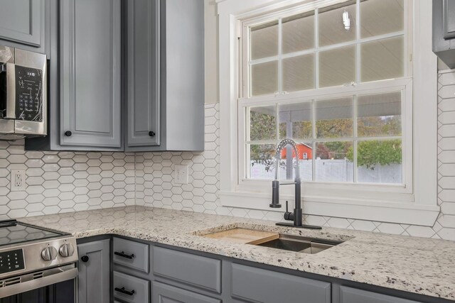 kitchen with backsplash, appliances with stainless steel finishes, a sink, and gray cabinetry