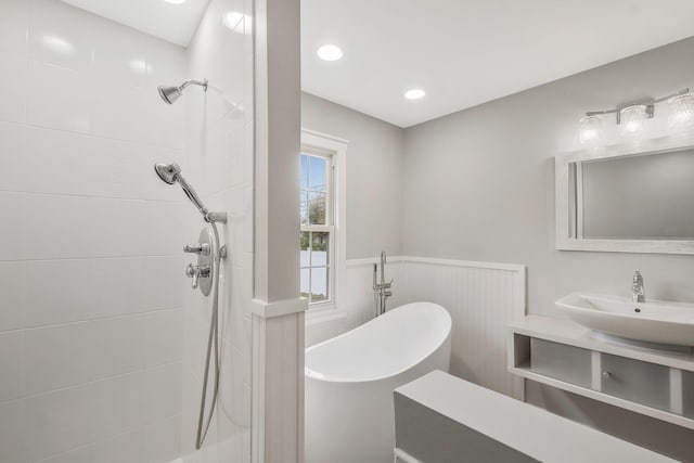 full bathroom featuring wainscoting, a tile shower, a soaking tub, and a sink