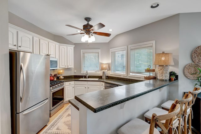 kitchen featuring a breakfast bar, a peninsula, dark countertops, appliances with stainless steel finishes, and a sink