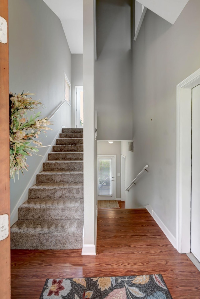 staircase featuring visible vents, a high ceiling, baseboards, and wood finished floors