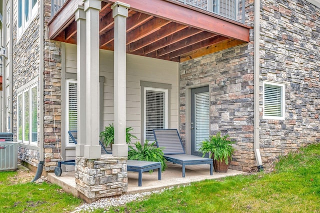doorway to property featuring a porch, central AC unit, and stone siding