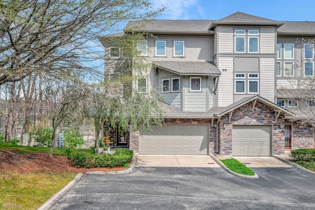 townhome / multi-family property featuring an attached garage, roof with shingles, driveway, and stone siding