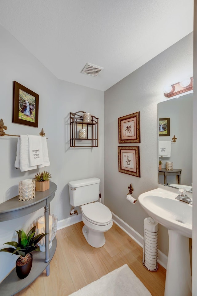 half bath with baseboards, toilet, visible vents, a sink, and wood finished floors