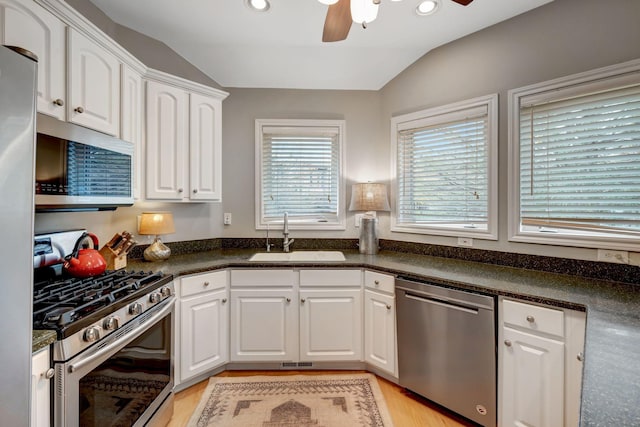kitchen featuring vaulted ceiling, a ceiling fan, dark countertops, appliances with stainless steel finishes, and a sink
