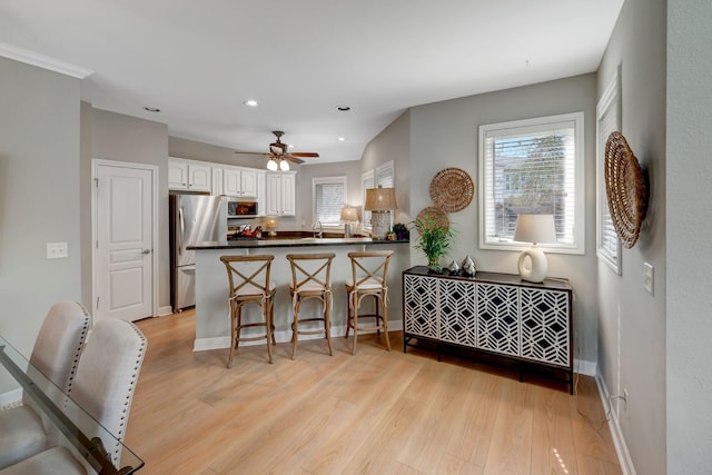 kitchen featuring white cabinets, appliances with stainless steel finishes, dark countertops, a peninsula, and light wood-style floors