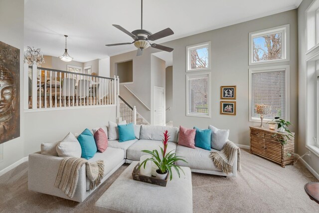 carpeted living area with baseboards, a ceiling fan, and stairs