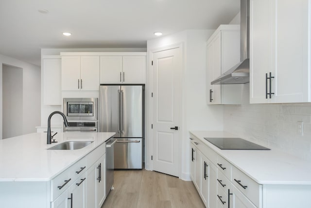 kitchen with a sink, light wood-style floors, light countertops, wall chimney exhaust hood, and appliances with stainless steel finishes