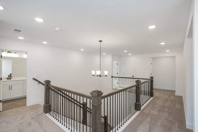 corridor featuring visible vents, baseboards, a chandelier, carpet flooring, and an upstairs landing