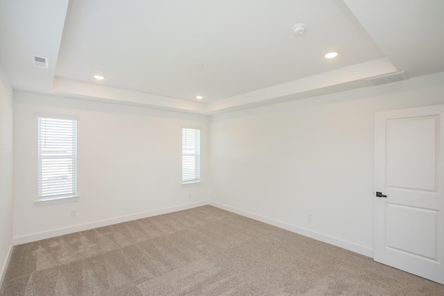 carpeted empty room featuring a tray ceiling, visible vents, and a wealth of natural light