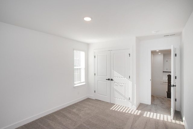unfurnished bedroom featuring light colored carpet, baseboards, visible vents, and a closet