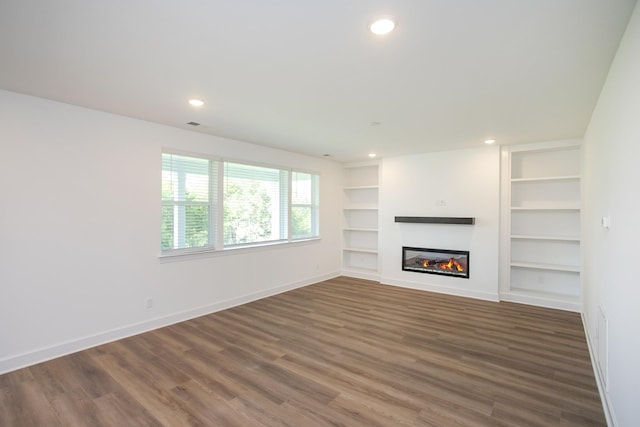 unfurnished living room with built in features, wood finished floors, baseboards, a glass covered fireplace, and recessed lighting