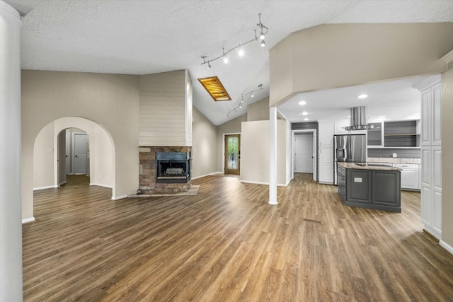 unfurnished living room featuring baseboards, vaulted ceiling, a fireplace, a textured ceiling, and wood finished floors