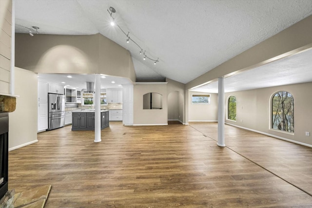 unfurnished living room featuring baseboards, high vaulted ceiling, wood finished floors, and a textured ceiling