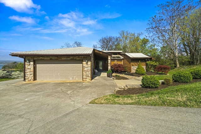 view of front facade featuring an attached garage, stone siding, metal roof, and concrete driveway