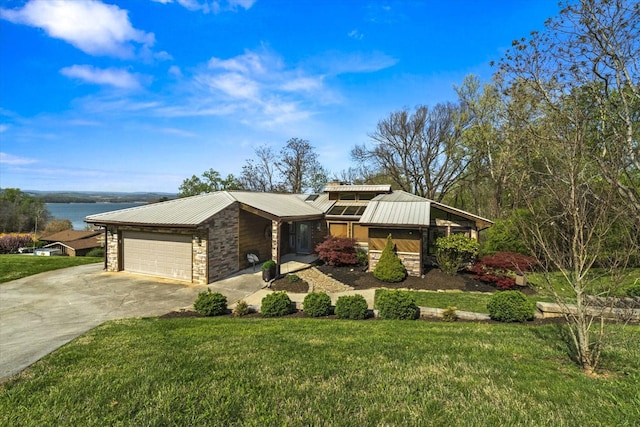 mid-century modern home featuring a front yard, stone siding, metal roof, and concrete driveway