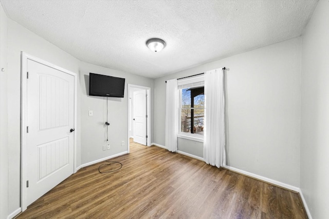 unfurnished bedroom featuring a textured ceiling, wood finished floors, and baseboards