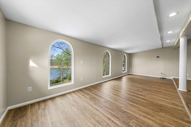 unfurnished living room featuring recessed lighting, baseboards, ornate columns, and wood finished floors