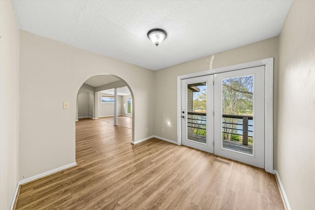spare room featuring visible vents, baseboards, arched walkways, a textured ceiling, and wood finished floors