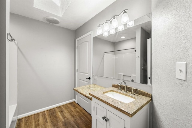 full bathroom with vanity, a skylight, wood finished floors, walk in shower, and baseboards