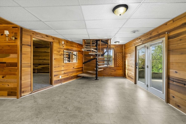 below grade area featuring wooden walls, a drop ceiling, and stairway