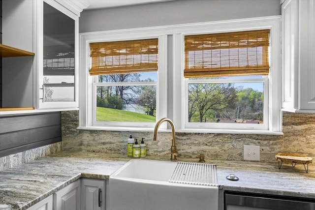 kitchen with decorative backsplash, a sink, light stone counters, and a healthy amount of sunlight
