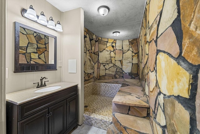 bathroom featuring a textured ceiling, tiled shower, vanity, and tile patterned floors