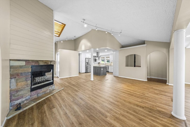 unfurnished living room featuring light wood-style floors, ornate columns, a textured ceiling, a stone fireplace, and baseboards