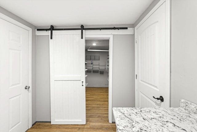 unfurnished bedroom with a walk in closet, a barn door, and wood finished floors