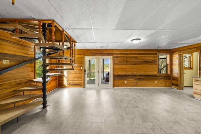 unfurnished living room with wood walls, stairway, and a paneled ceiling