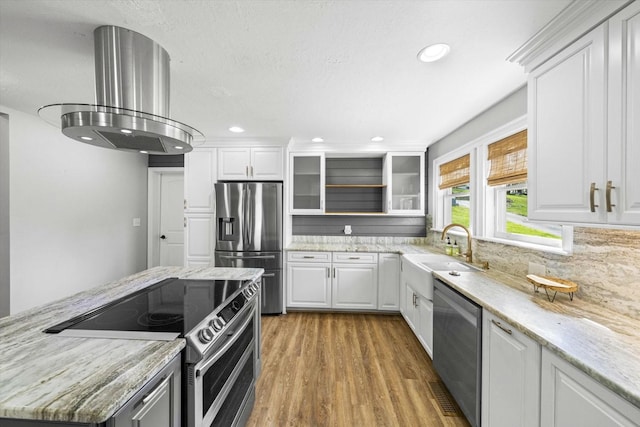 kitchen featuring tasteful backsplash, glass insert cabinets, appliances with stainless steel finishes, island exhaust hood, and light wood-style flooring