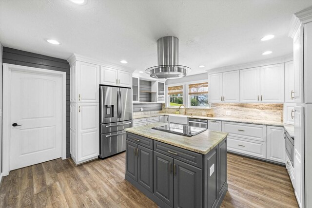 kitchen with appliances with stainless steel finishes, wood finished floors, wall chimney range hood, and white cabinetry