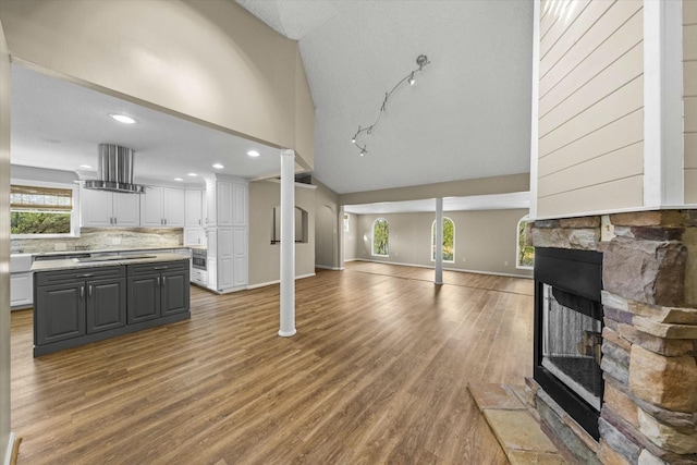 living area featuring baseboards, a stone fireplace, recessed lighting, wood finished floors, and high vaulted ceiling