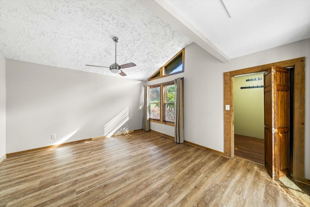 interior space with baseboards, a textured ceiling, a ceiling fan, vaulted ceiling with beams, and wood finished floors