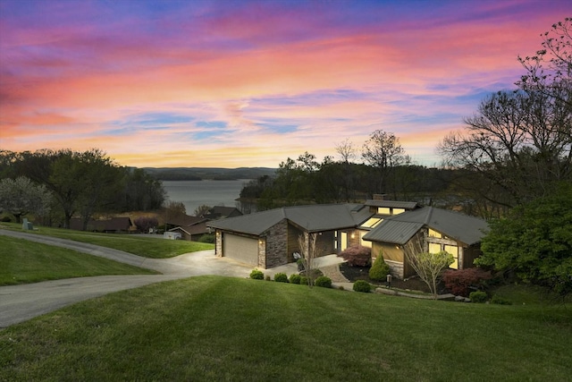 view of front of property featuring driveway, stone siding, a garage, metal roof, and a lawn