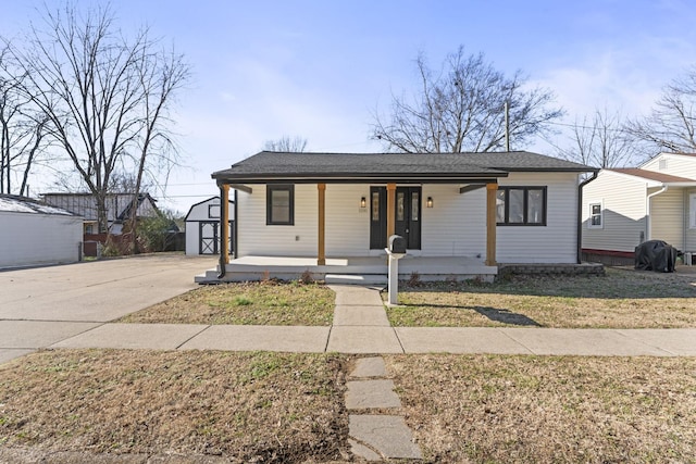 bungalow featuring concrete driveway, roof with shingles, an outbuilding, and covered porch