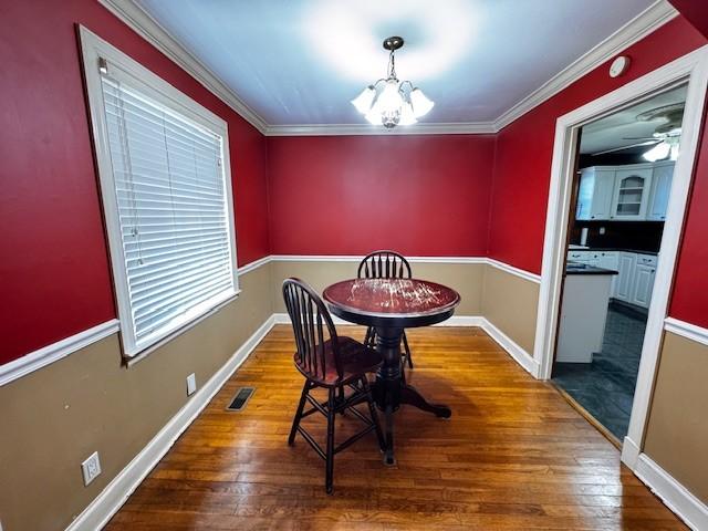 dining area featuring a chandelier, hardwood / wood-style floors, crown molding, and visible vents