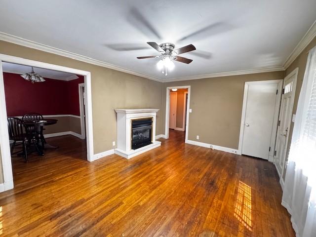 unfurnished living room featuring baseboards, ceiling fan with notable chandelier, crown molding, and wood finished floors