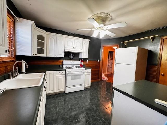 kitchen with white appliances, a ceiling fan, white cabinetry, a sink, and dark countertops