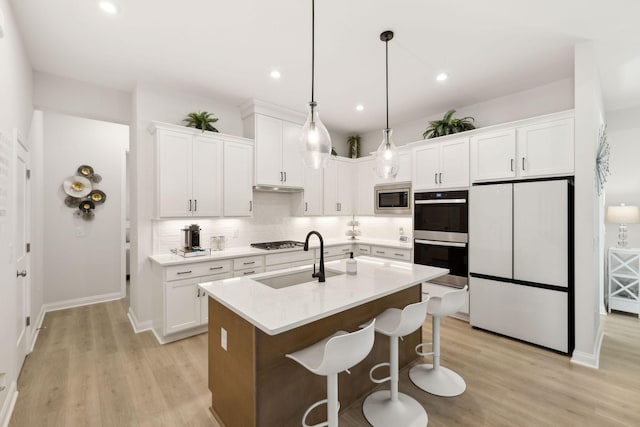 kitchen with decorative backsplash, white cabinets, a sink, light wood-style flooring, and stainless steel appliances