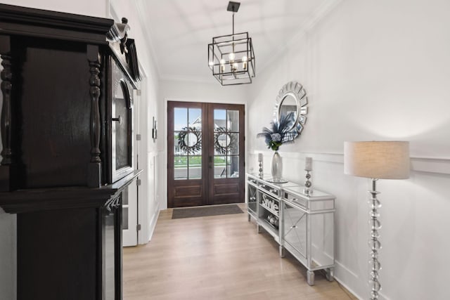 entryway with crown molding, an inviting chandelier, light wood-style floors, and french doors