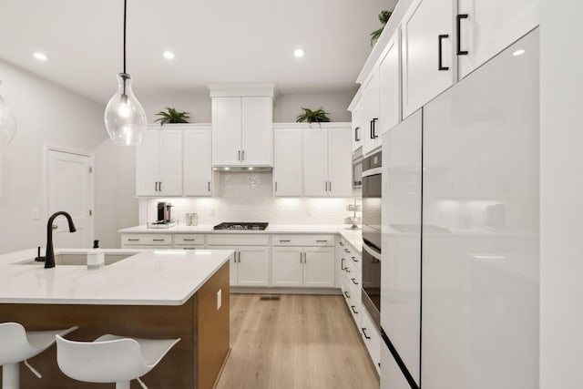 kitchen featuring decorative backsplash, light wood-style floors, a sink, white fridge, and stainless steel gas stovetop