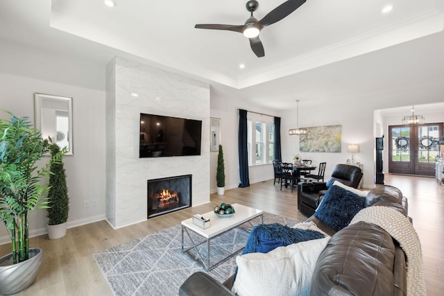 living area with ceiling fan with notable chandelier, a tray ceiling, and a wealth of natural light