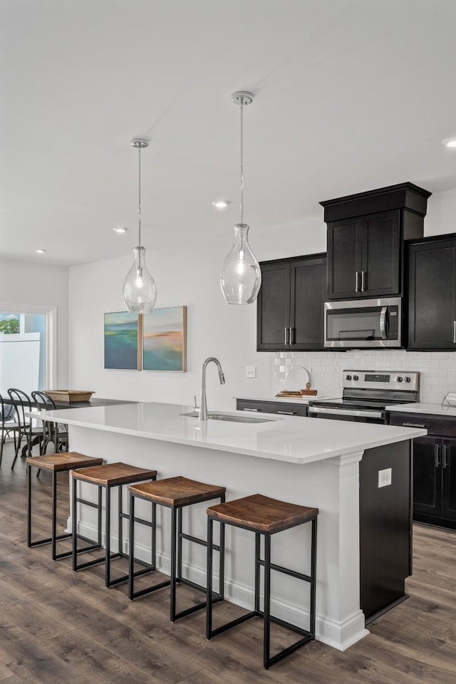 kitchen featuring dark wood finished floors, dark cabinets, a large island, appliances with stainless steel finishes, and a sink