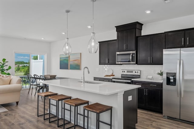 kitchen featuring an island with sink, backsplash, dark wood-type flooring, stainless steel appliances, and a sink