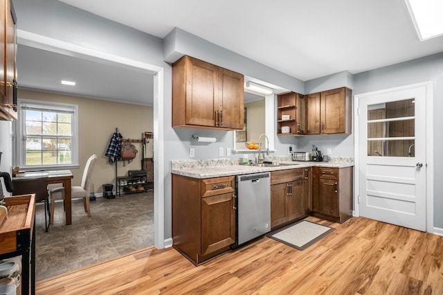 kitchen with light wood finished floors, stainless steel dishwasher, a sink, and open shelves