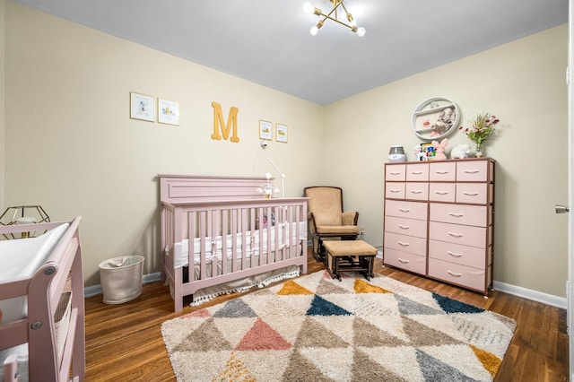 bedroom with wood finished floors, baseboards, a notable chandelier, and a crib