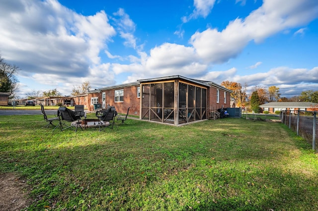 rear view of property with a fire pit, brick siding, a fenced backyard, a sunroom, and a lawn