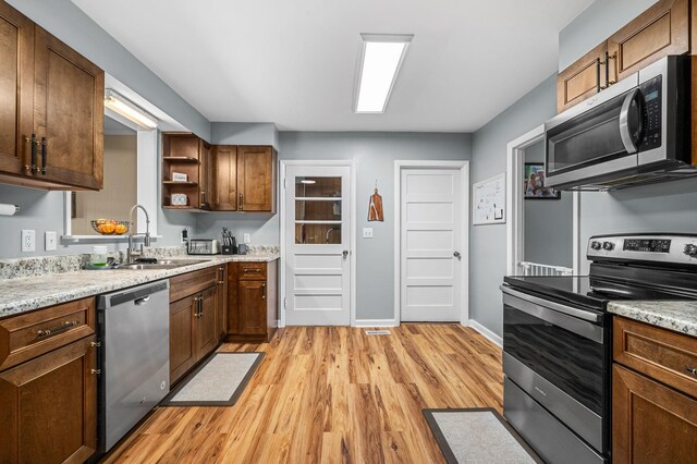 kitchen featuring baseboards, light wood-type flooring, open shelves, appliances with stainless steel finishes, and a sink