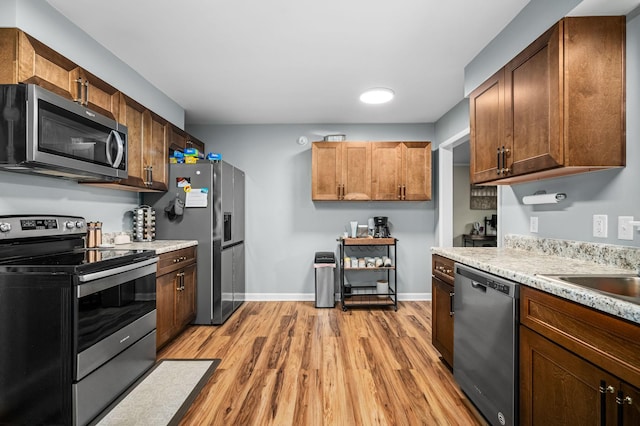 kitchen with stainless steel appliances, light wood-style flooring, baseboards, and a sink