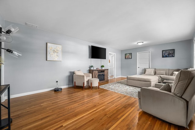 living room featuring a fireplace, visible vents, baseboards, and wood finished floors
